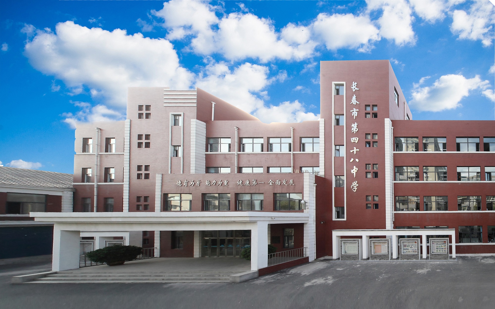 长春市第四十八中学教学楼全景,红褐色校舍前设有主入口,背景为蓝天白云