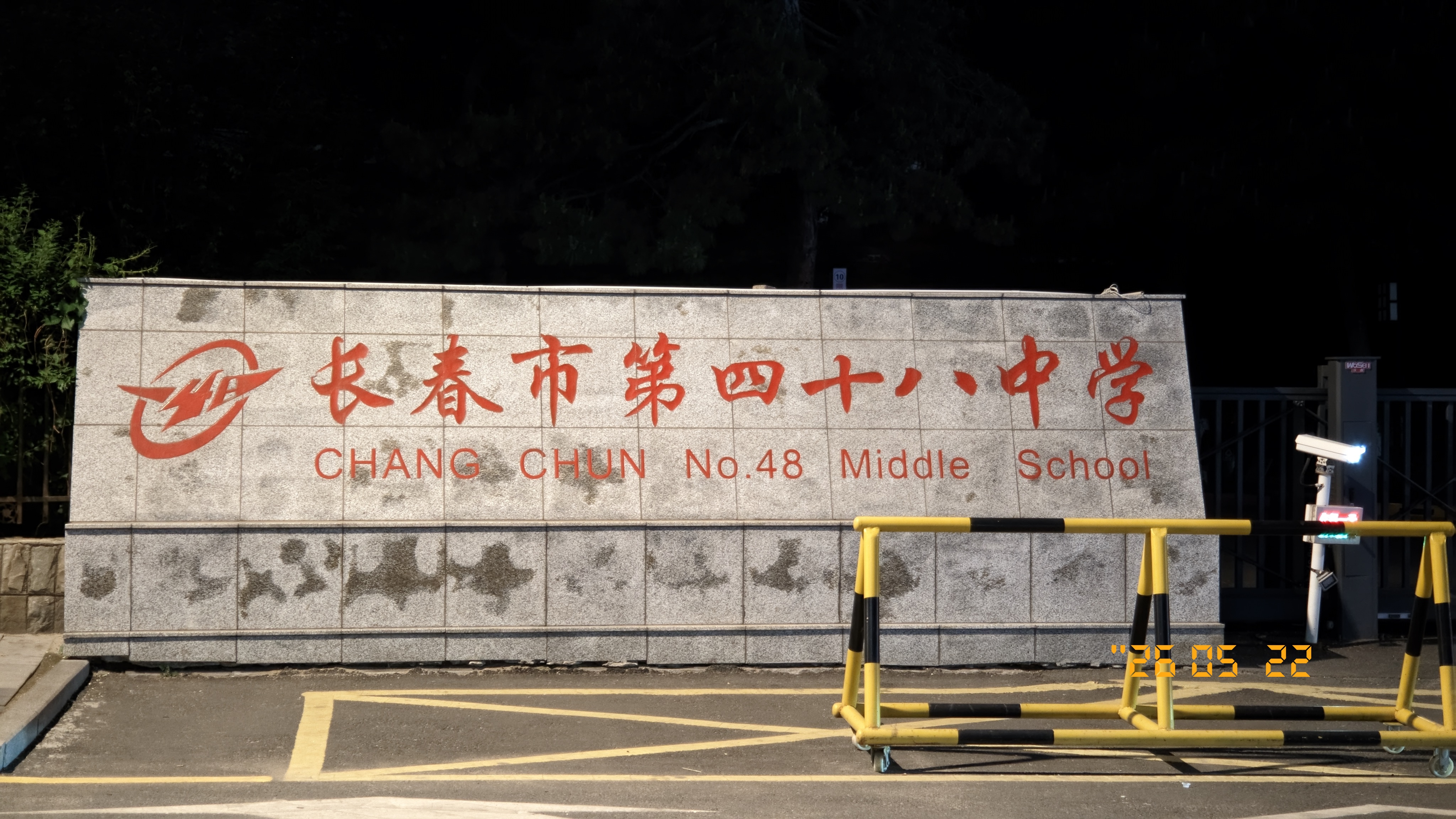 夜间灯光下的长春市第四十八中学校名墙,灰色石墙上有红色中文校名和英文名称